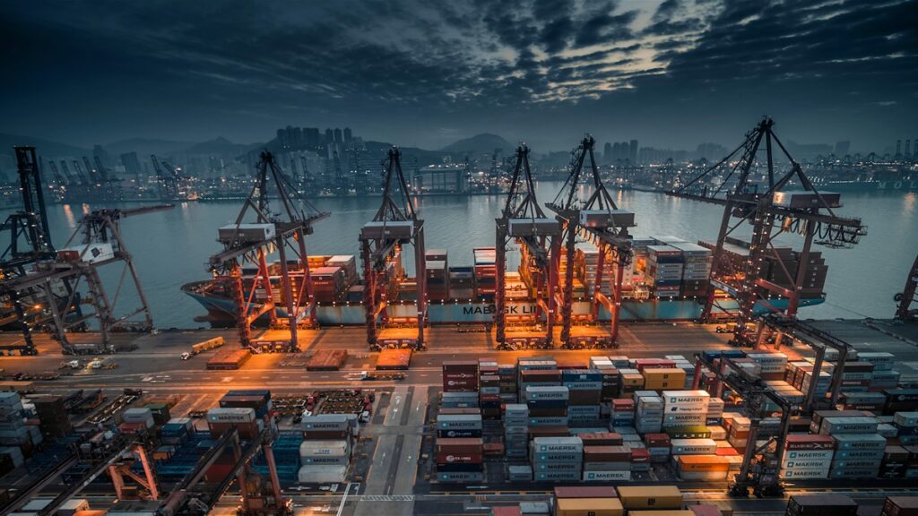 Container ship loaded by cranes at a busy port at dusk